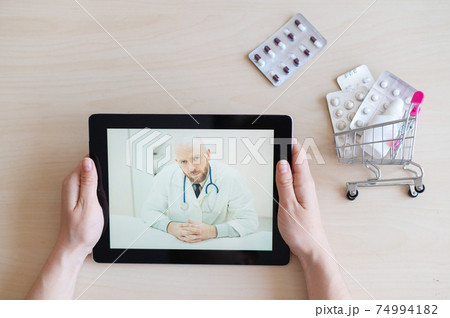 The patient communicates with a male therapist via video chat on a digital tablet. Woman at online consultation with a doctor. Online pharmacy concept. Mini medicine trolley. The patient communicates with a male therapist via video chat on a digital tablet. Woman at online consultation with a doctor. Online pharmacy concept. Mini medicine trolley. 74994182