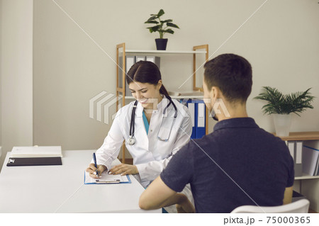 Friendly practitioner smiling and writing down prescription for young male patient 75000365