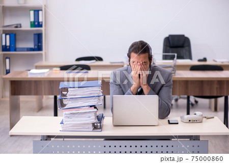 Young male employee unhappy with excessive work in the office Young male employee unhappy with excessive work in the office 75000860