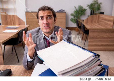 Young male employee unhappy with excessive work in the office Young male employee unhappy with excessive work in the office 75001648
