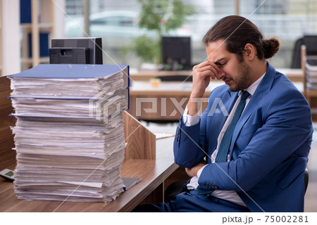 Young male employee unhappy with excessive work in the office 75002281
