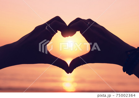 Woman hand do heart shape on sunset sky and bokeh background. love and valentine day. 75002364