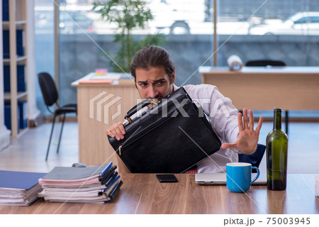Young male alcohol addicted employee working in the office Young male alcohol addicted employee working in the office 75003945