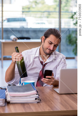 Young male alcohol addicted employee working in the office 75003960