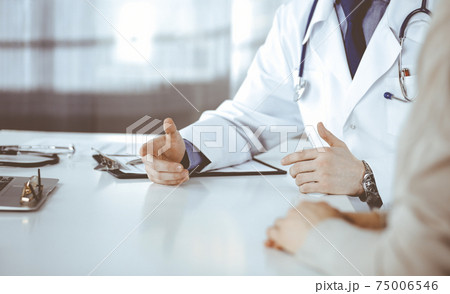Unknown male doctor and patient woman discussing something while sitting in clinic and using clipboard. Best medical service in hospital, medicine, pandemic stop Unknown male doctor and patient woman discussing something while sitting in clinic and using clipboard. Best medical service in hospital, medicine, pandemic stop 75006546