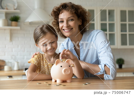 Happy smiling mom cuddling small girl putting coin to piggybank. Happy smiling mom cuddling small girl putting coin to piggybank. 75006747