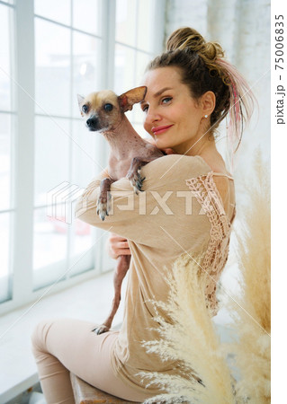 Happy adult woman hugging dog in room near big window Happy adult woman hugging dog in room near big window 75006835