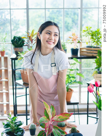 Happy beauty woman Portarit of positive cheerful floral entrepreneur concept wear apron beautiful flower plants indoors garden Happy beauty woman Portarit of positive cheerful floral entrepreneur concept wear apron beautiful flower plants indoors garden 75009992