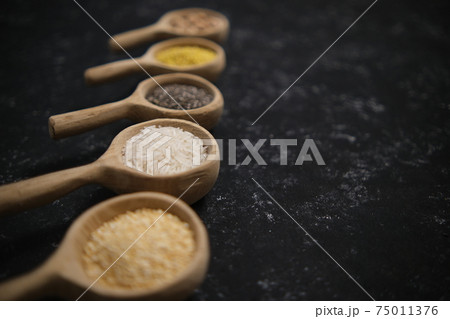 Spices. Chia seeds, millet, rice, chickpeas, quinoa in a wooden spoon on a black and gray background. Five spoons in a row. Selective soft focus Spices. Chia seeds, millet, rice, chickpeas, quinoa in a wooden spoon on a black and gray background. Five spoons in a row. Selective soft focus 75011376