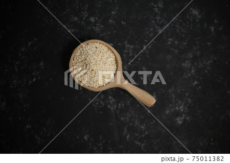 Spices. Sesame seeds in a wooden spoon on a black and gray background. Top view Spices. Sesame seeds in a wooden spoon on a black and gray background. Top view 75011382