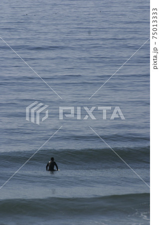 A surfer lying on his surfboard paddles over an approaching wave on a beach in Portugal on the Atlantic Ocean 75013333