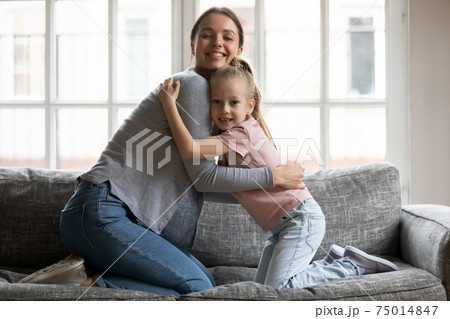 Happy mom cuddling little daughter girl on sofa Happy mom cuddling little daughter girl on sofa 75014847