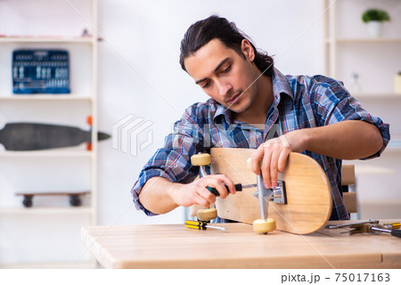 Young man repairing skateboard at workshop 75017163