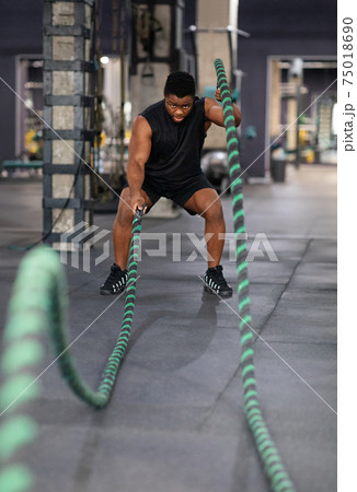 Muscular black guy having work out with ropes at gym 75018690