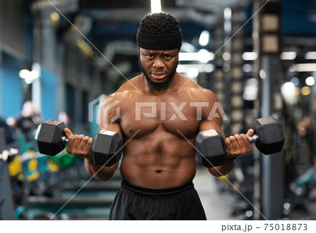 Muscular black guy doing workout with dumbbells at gym Muscular black guy doing workout with dumbbells at gym 75018873