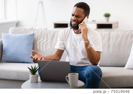 Black Man Talking On Phone Having Problem With Laptop Indoor 75019046