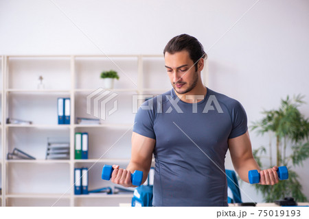 Young handsome employee doing sport exercises in the office Young handsome employee doing sport exercises in the office 75019193