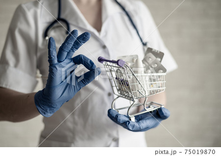 A faceless female pharmacist holds a mini shopping cart with medications and gestures with the ok. Taking vitamins is the key to good health. Doctor's recommendations. A faceless female pharmacist holds a mini shopping cart with medications and gestures with the ok. Taking vitamins is the key to good health. Doctor's recommendations. 75019870