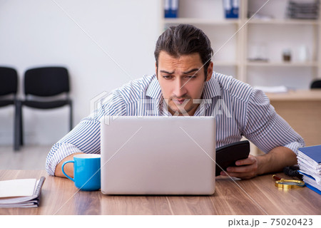 Young male bookkeeper working in the office Young male bookkeeper working in the office 75020423