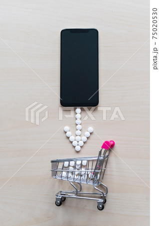 Online pharmacy concept. Buying medicine online over the phone. Delivery of pharmaceuticals. Mini trolley with capsules and a smartphone with a black blank screen. 75020530