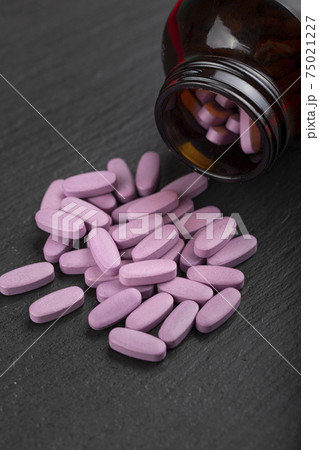 Pink pills are scattered from a glass jar on a black background.  Health care concept.  75021227