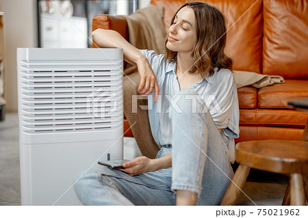 Woman sitting near air purifier and moisturizer appliance Woman sitting near air purifier and moisturizer appliance 75021962