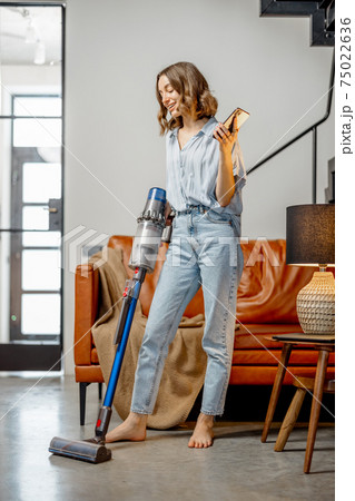 Woman with cordless vacuum cleaning floor at home  75022636
