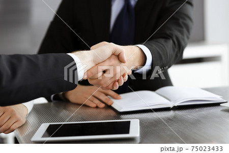 Unknown businessmen shaking hands above the glass desk in a modern office, close-up. Unknown business people at meeting. Teamwork, partnership and handshake concept 75023433