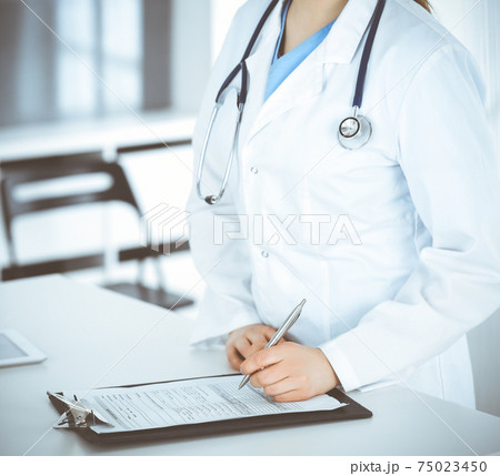Unknown woman-doctor or internal student filling up medical documents while standing in clinic reception desk. Data in medicine 75023450