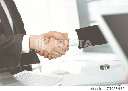 Unknown diverse business people are shaking hands finishing up meeting at the desk in office, close-up. Handshake concept 75023472