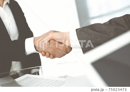Unknown diverse business people are shaking hands finishing up meeting at the desk in office, close-up. Handshake concept 75023473