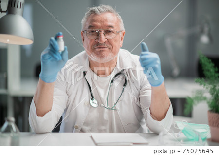 An experienced medical specialist in the office recommends to his patients the latest coronavirus vaccine in a glass ampoule An experienced medical specialist in the office recommends to his patients the latest coronavirus vaccine in a glass ampoule 75025645