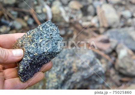 Fingers holding chromite ore over out of focus rocks background Fingers holding chromite ore over out of focus rocks background 75025860
