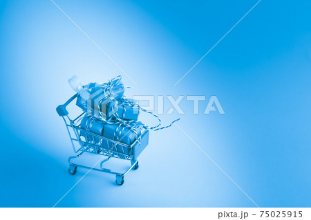 Pile of wrapped gift boxes in shopping trolley cart on blue background. Pile of wrapped gift boxes in shopping trolley cart on blue background. 75025915