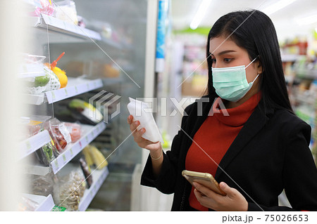 Young smart business asian woman wearing face mask looking and choosing grocery to buy from shelf in supermarket department store or shopping mall, new normal coronavirus crisis or covid19 outbreak.. 75026653