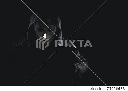 Dangerous anonymous hacker man in black hooded, white mask use computer and mobile phone, break security data corporate server. He working on black background. Internet crime, cyber attack security. 75026688