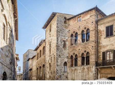 Old houses of different ages merged into one wall on Piazza Della Cisterna in San Gimignano, Italy 75035409
