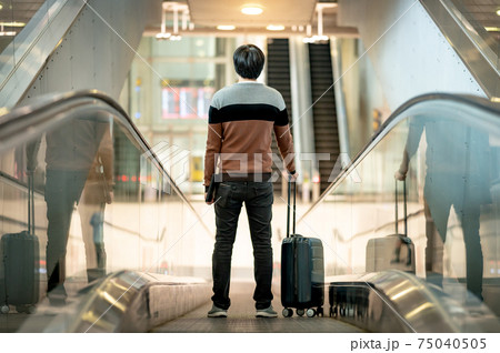 Male tourist carrying suitcase luggage on travelator Male tourist carrying suitcase luggage on travelator 75040505