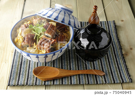 ランチョンマットの上の鰻蒲焼きを卵でとじたうな玉丼とお吸い物のセットと木製スプーン 75040945