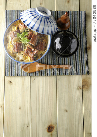 ランチョンマットの上の鰻蒲焼きを卵でとじた熱々うな玉丼とお吸い物のセットと木製スプーンを俯瞰で撮影 75040989
