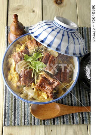 ランチョンマットの上の鰻蒲焼きを卵でとじた熱々うな玉丼とお吸い物のセットと木製スプーンを俯瞰で撮影 75040990