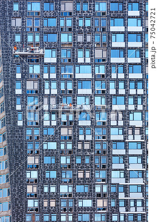 Fragment of the facade of a high-rise building under construction and its insulation using winches and mobile platforms, the concept of energy saving in residential construction. Fragment of the facade of a high-rise building under construction and its insulation using winches and mobile platforms, the concept of energy saving in residential construction. 75042721