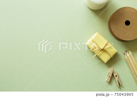 Gift box, string roll, wooden pencils, clips on green background. flat lay, top view, copy space 75043905