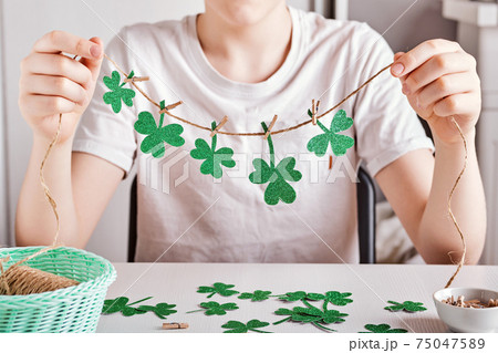DIY St.Patricks Day decor. Happy boy make garland of shiny green paper. Selective focus 75047589