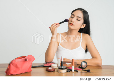 Beautiful young woman applying foundation powder or blush with makeup brush. Mixed race Asian Caucasian model. 75049352