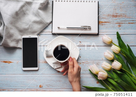 bouquet of white tulips with a Cup of coffee in women's hands, a smartphone and an empty notebook for text 75051411