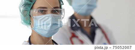 Two doctors in glasses and protective medical masks stand in office Two doctors in glasses and protective medical masks stand in office 75052007