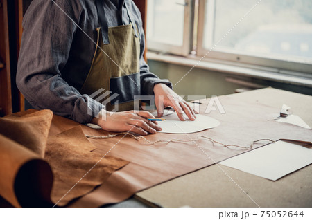 In the boot shop, an experienced shoemaker starts the process of producing shoes, makes a pattern on the skin In the boot shop, an experienced shoemaker starts the process of producing shoes, makes a pattern on the skin 75052644