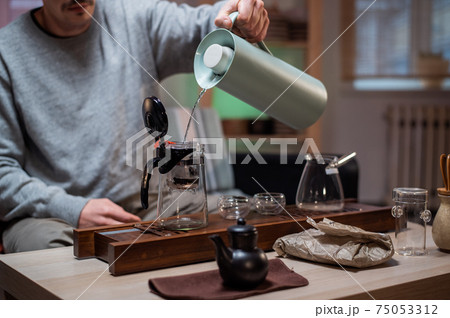 A true master of traditional chinese ceremonies brews aged raw black tea by pouring hot water into the teapot. Tea party in the comfort of home. A true master of traditional chinese ceremonies brews aged raw black tea by pouring hot water into the teapot. Tea party in the comfort of home. 75053312