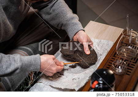 Shot without a face. Close-up of the master's hands picking a tea cake with a needle for a tea ceremony or chinese tea tasting. Shot without a face. Close-up of the master's hands picking a tea cake with a needle for a tea ceremony or chinese tea tasting. 75053318